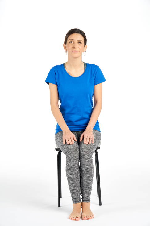 Frau sitzt mit leicht abfallenden Oberschenkeln auf einem Stuhl