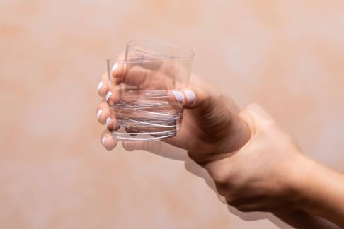 Mensch mit Parkinson hebt ein Wasserglas