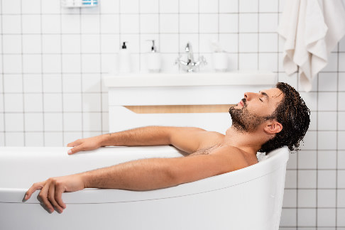 Mann liegt mit geschlossenen Augen in der Badewanne um die Oberschenkelschmerzen zu behandeln